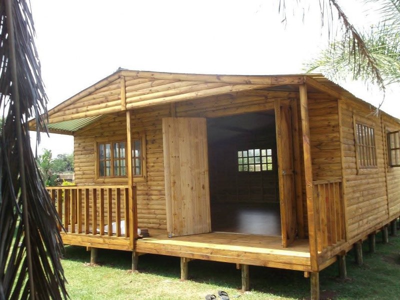 Large wooden Wendy house with front porch and open door, built on stilts in a grassy yard