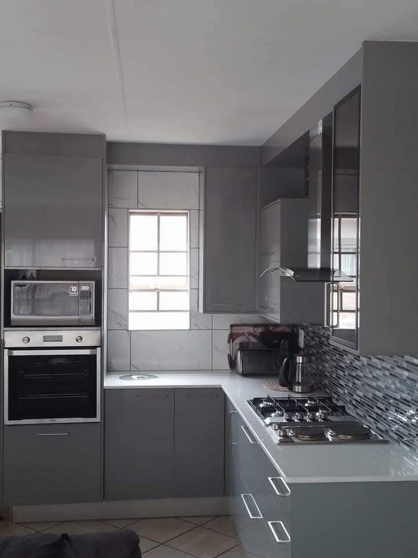 Modern grey kitchen renovation with built-in oven, gas stove, and tiled backsplash.