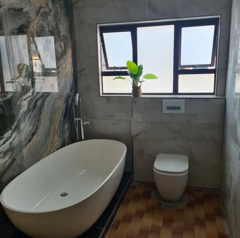Modern renovated bathroom with freestanding bathtub, marble wall, and frosted window.