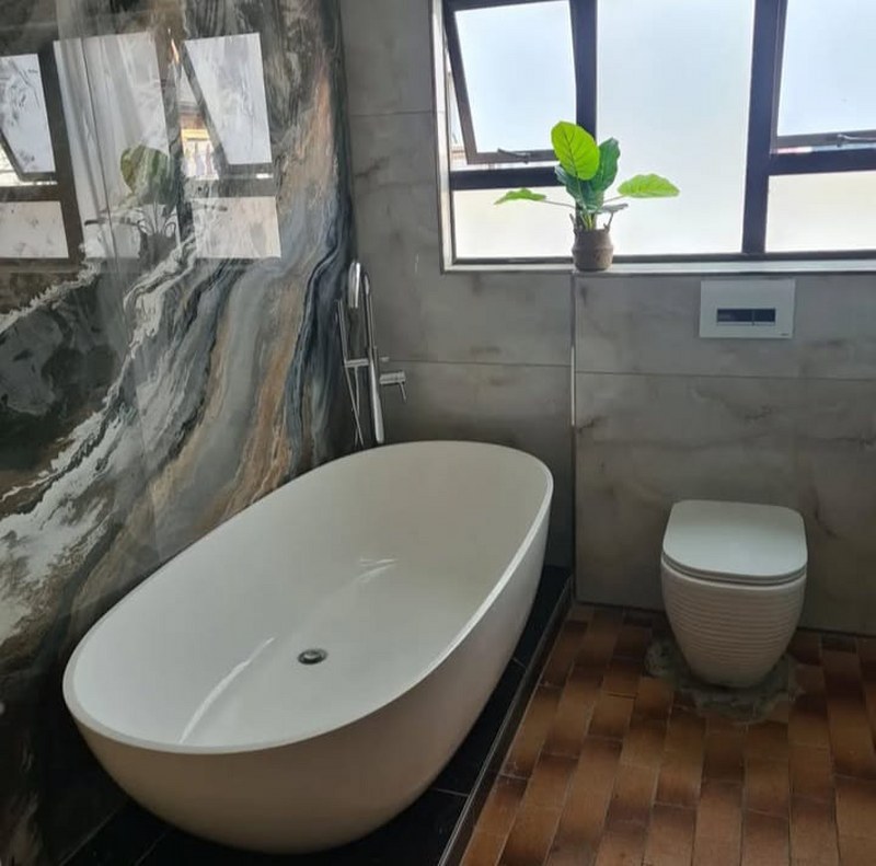 Modern bathroom renovation with a freestanding bathtub, marble wall, and large frosted window.