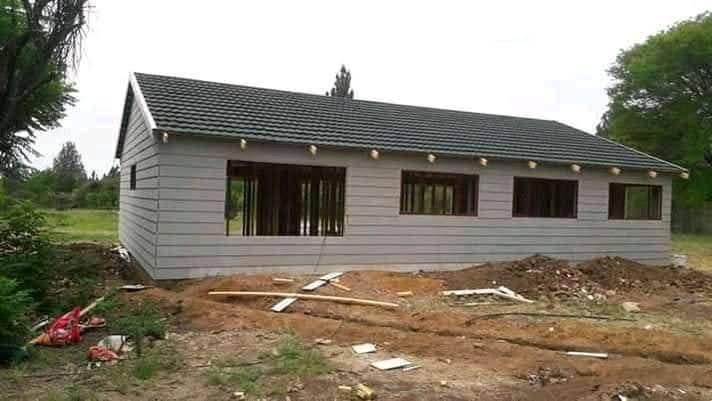 Large Wendy house structure under construction with multiple window openings and a tiled roof on a rural plot.